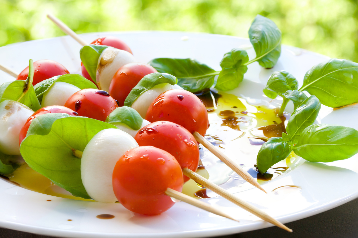 Plate of tomatoes, mozzarella balls, and basil on skewers in outdoor setting
